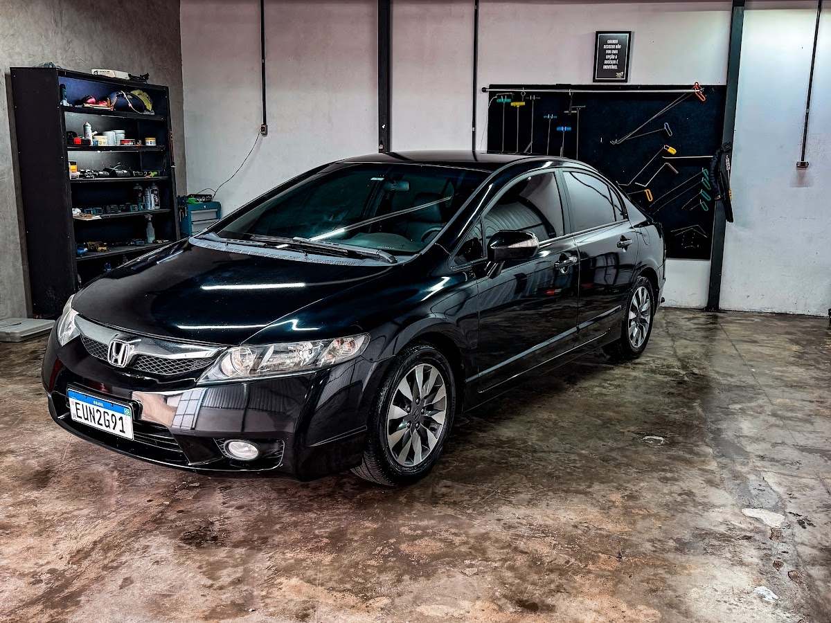 Interior da oficina Marquinhos com Honda Civic preto e painel de ferramentas de martelinho de ouro na parede
